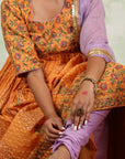 A women wearing Orange Anarkali Kurta Set with Purple Dupatta.