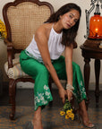 A woman sitting on a chair and wearing white and green co-ord set with flowers in her hand.