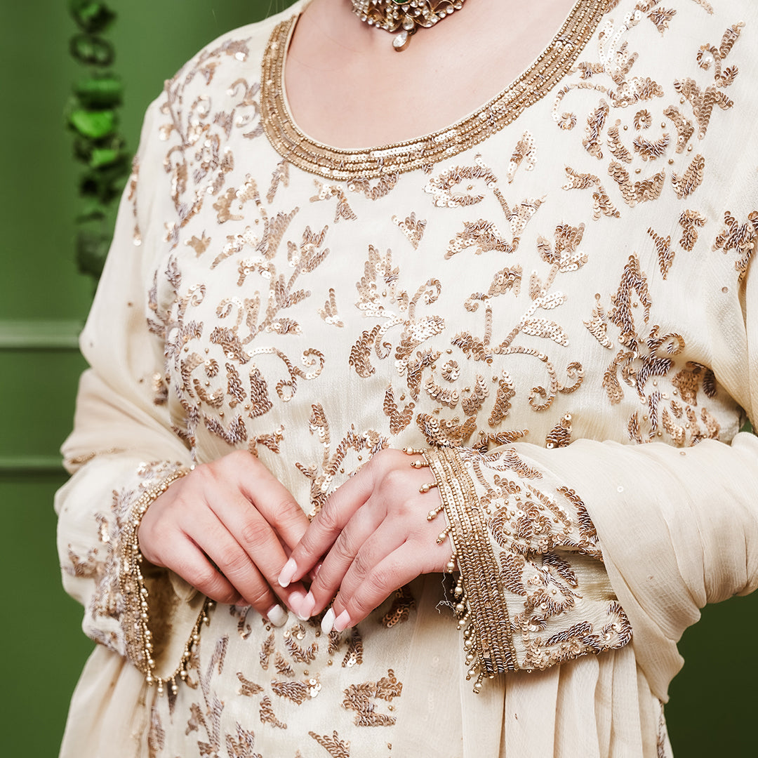 A women wearing beige colored Sharara Suit Set with Dupatta.