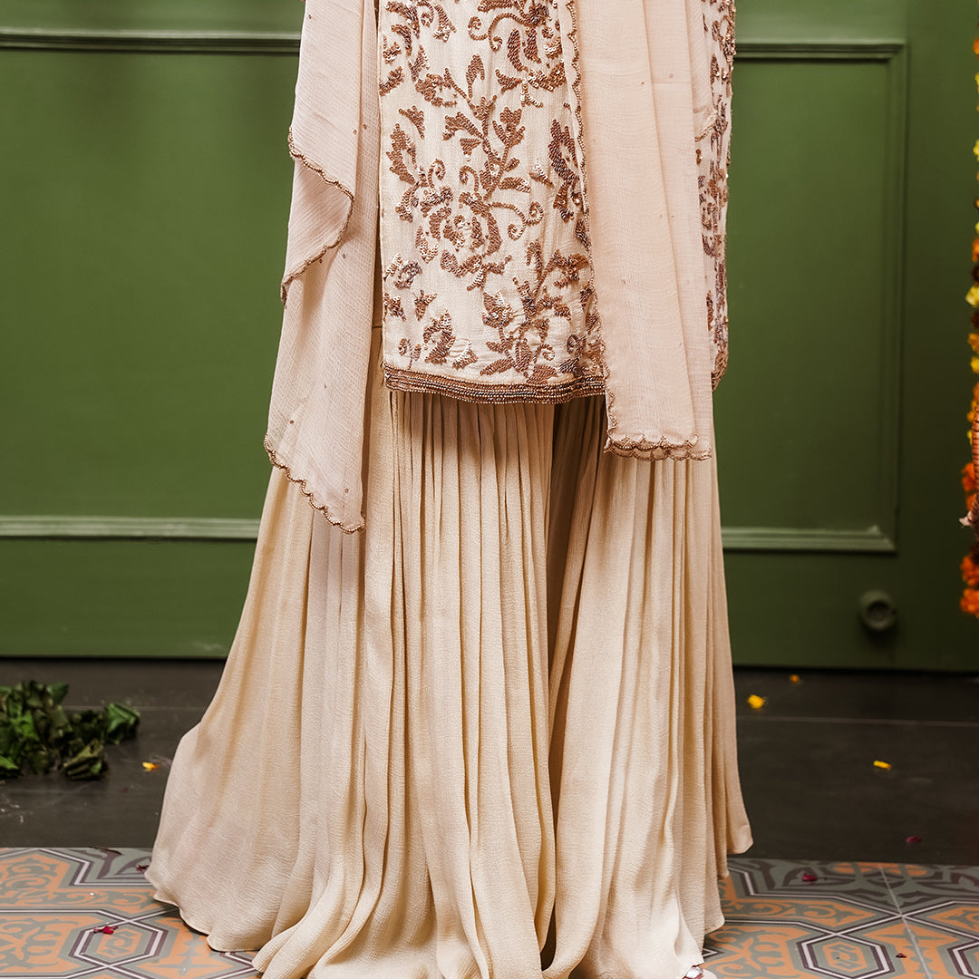 A women wearing beige colored Sharara Suit Set with Dupatta.