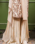 A women wearing beige colored Sharara Suit Set with Dupatta.