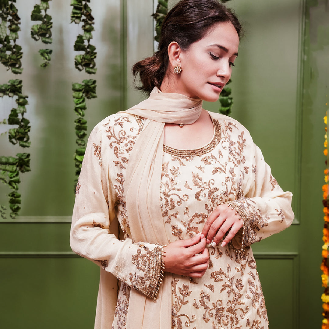 A women wearing beige colored Sharara Suit Set with Dupatta.