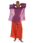 A woman wearing Purple and Orange colored co-ord set with both her hands on head.